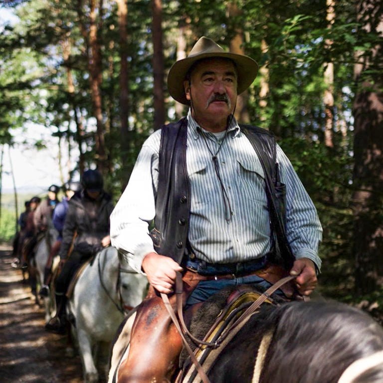 Mann mit Cowboyhut und Schnurrbart sitzt auf Pferd, hinter ihm andere Reiter. (Foto: SWR)