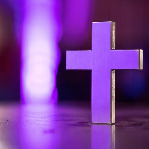 Ein weißes Kreuz schimmert in lilafarbenem Licht.